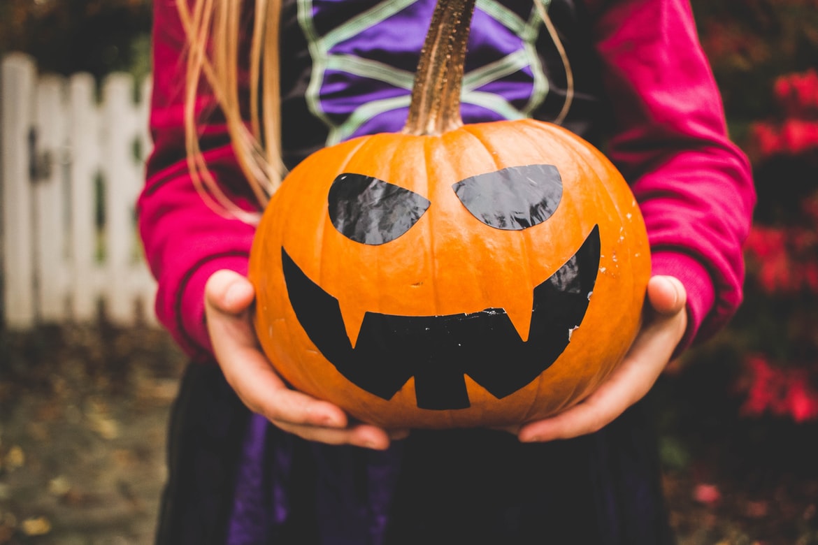 Niña disfrazada de bruja con una calabaza decorada para Halloween